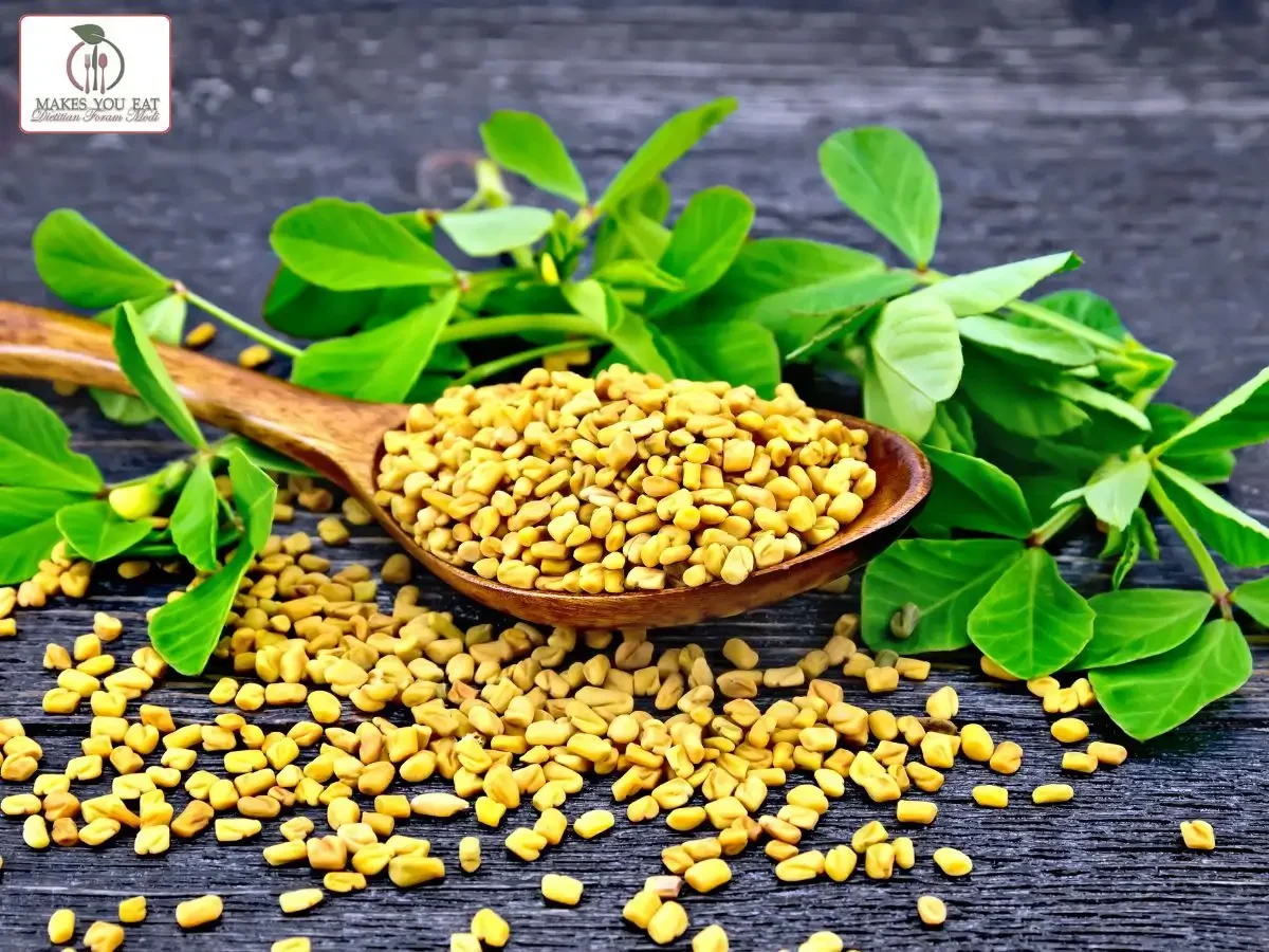 Fenugreek seeds in a spoon with leaves beside.